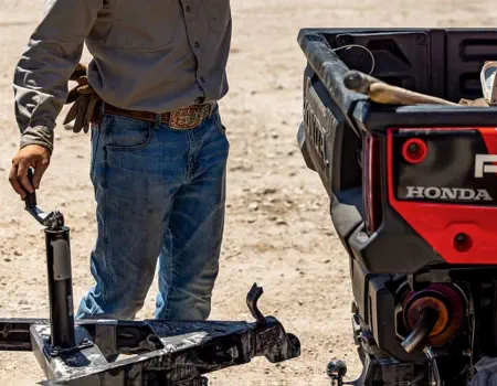 a man standing next to a trailer coupler/jack, working to connect it to the Honda vehicle